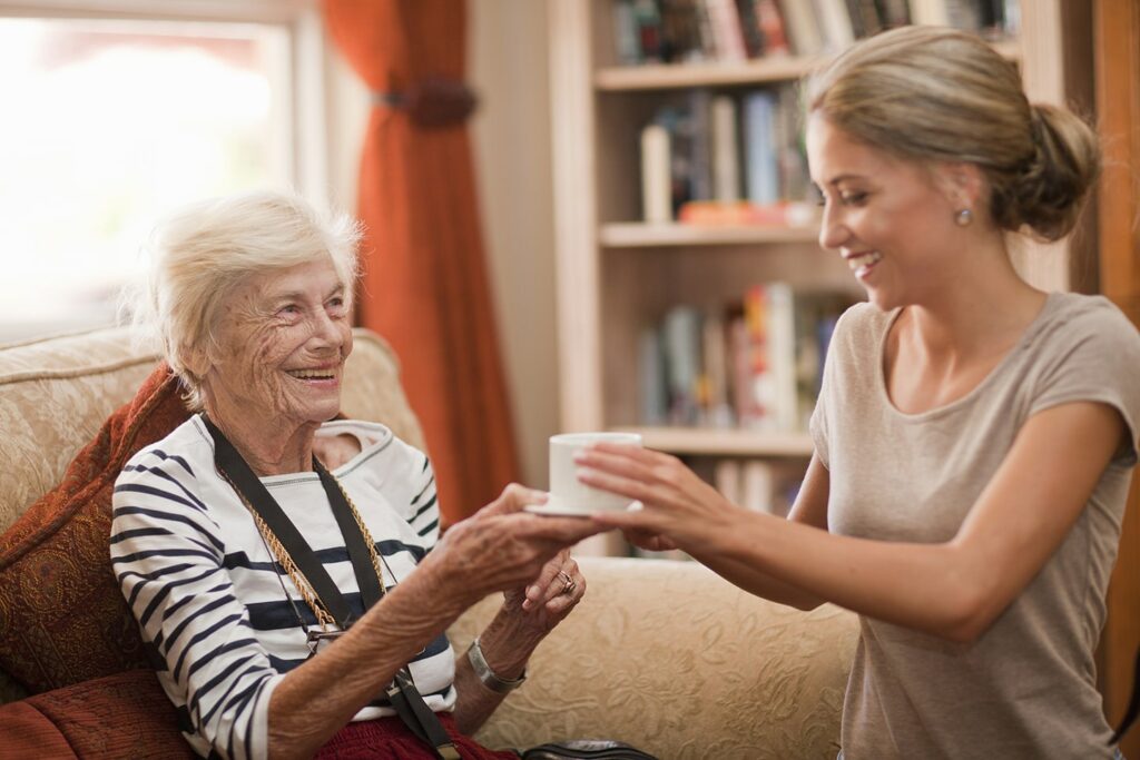 care-assistant-handing-coffee-cup-to-senior-woman-min